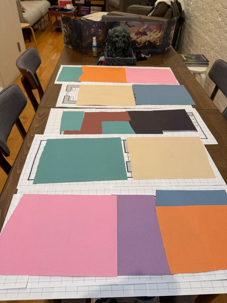 A printed out D&D dungeon hidden by construction paper fog of war on a large table with a DM screen at the end