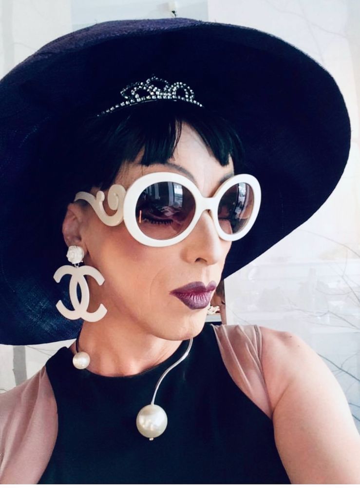 Foto von Herrn Fraumann mit Hut, Brille und Ohrgehängen von Coco Chanel. Im Ursprungsposting im Vergleich mit dem Foto von FLOTUS, die ihr Gesicht mit dem Hut verdeckt hatte.