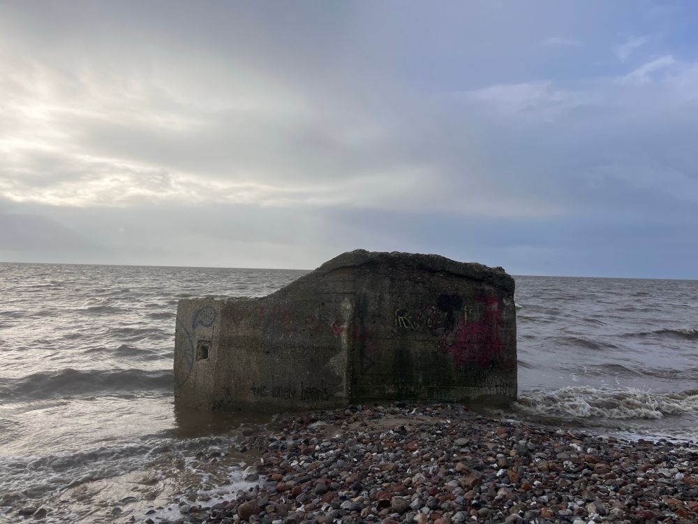 Ein Wellenbrecher am Strand dahinter das Meer . Die kleinen Wellen brechen am Stein . 