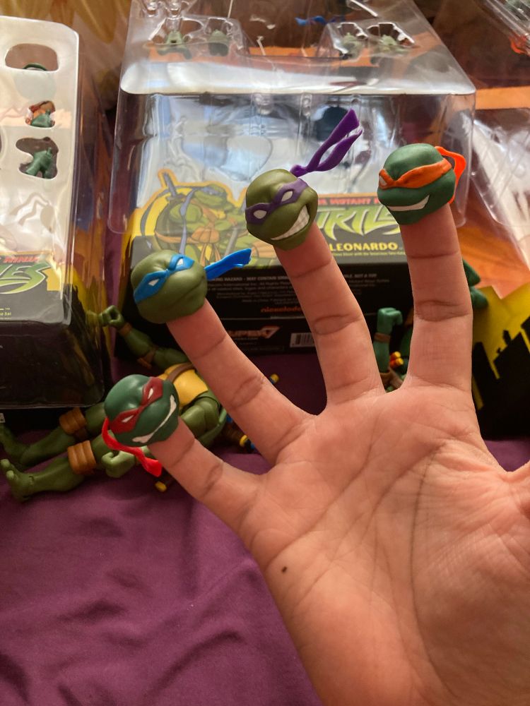 Picture of a hand palm up with tmnt2003 heads on their fingers like finger puppets