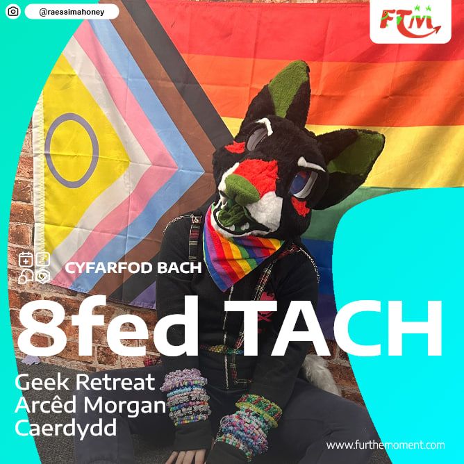 Siwt ffwr ddu, coch a gwyrdd yn eistedd ar y llawr o flaen baner Cynnydd. Maen nhw'n gwisgo Bandana Lliw Balchder.