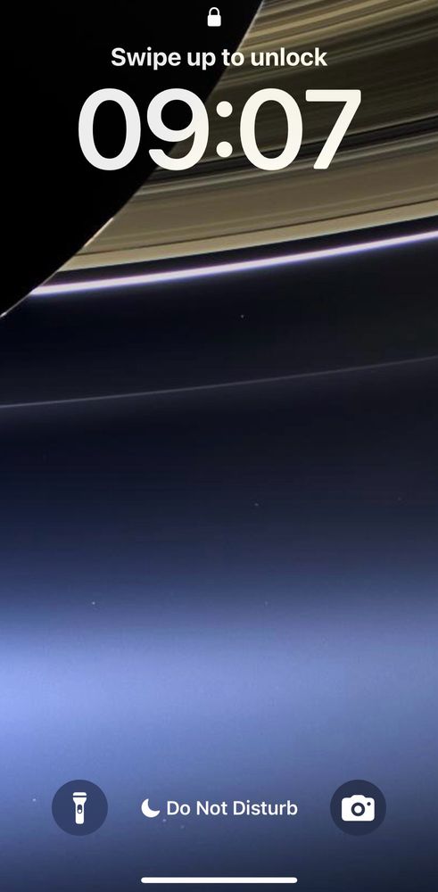 Phone lock screen showing the Cassini photo of Saturn and its rings in the upper left. The pale dot of Earth in the lower right and other stars against the glow of the spiral arm of the Milky Way. 
