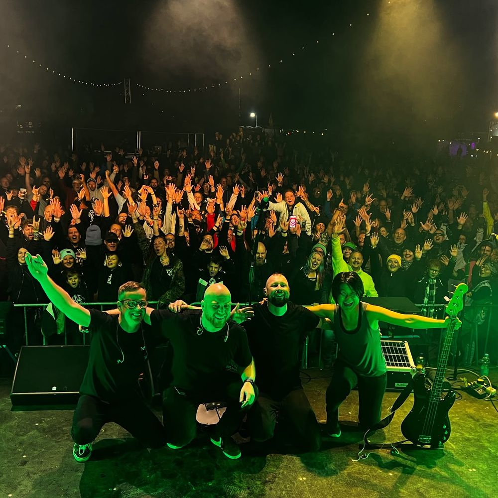 Männi und seine Band auf der Bühne. Im Hintergrund eine jubelnde Menschenmenge mit den Händen in der Luft.