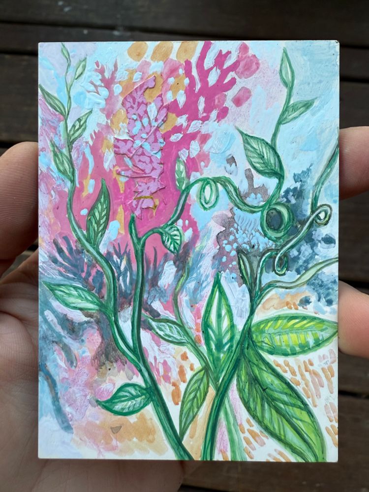 Hand holding a miniature painting of plants and abstraction with dominating colors: green, blue, pink, yellow ochre.