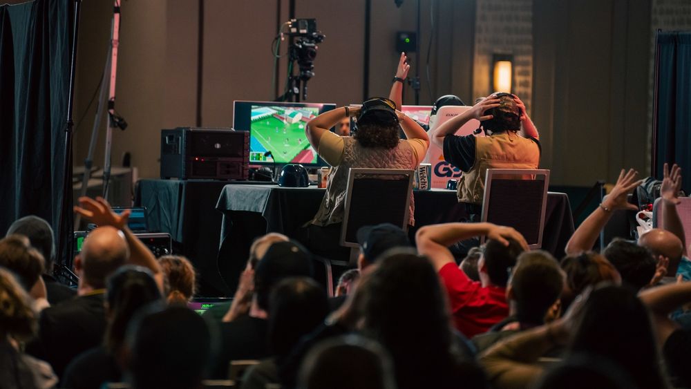 a photo of the gdq stage from the perspective of the audience, with two people (me and bryonato) reacting to what's on the screen