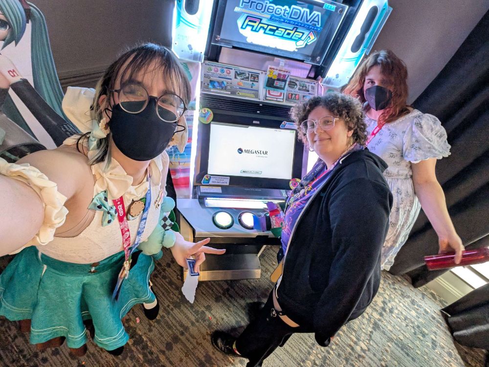 three people (evie, me, and casey) posing in front of a project diva arcade cabinet