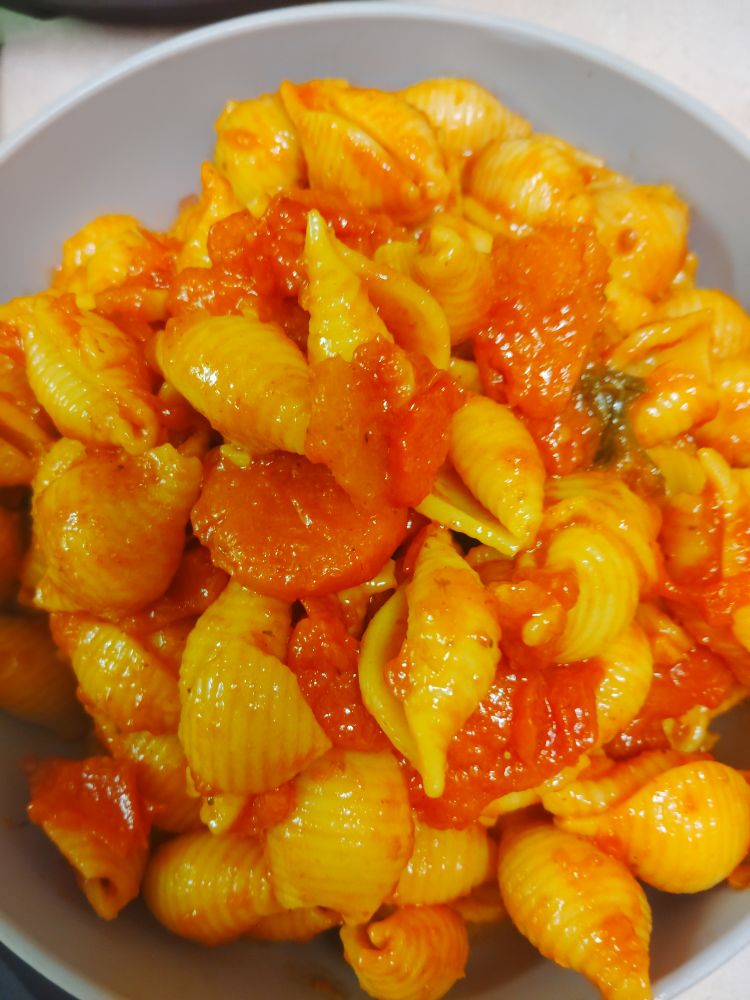 Shell pasta covered in sauce and cooked tomato pieces and carrot slices