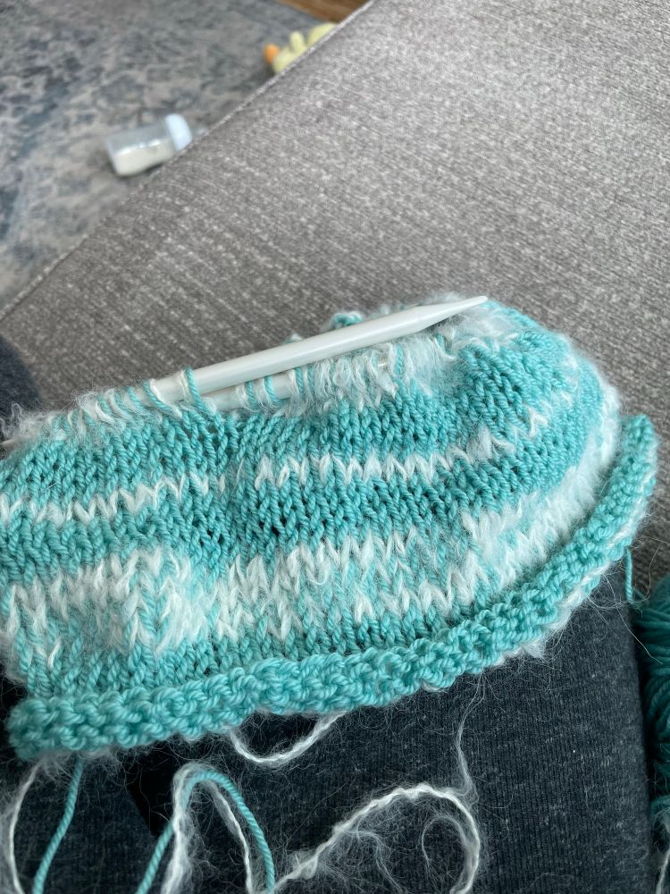 A pair of size 11 circular needles hold about six inches of blue and white stripes in straight stitch. 