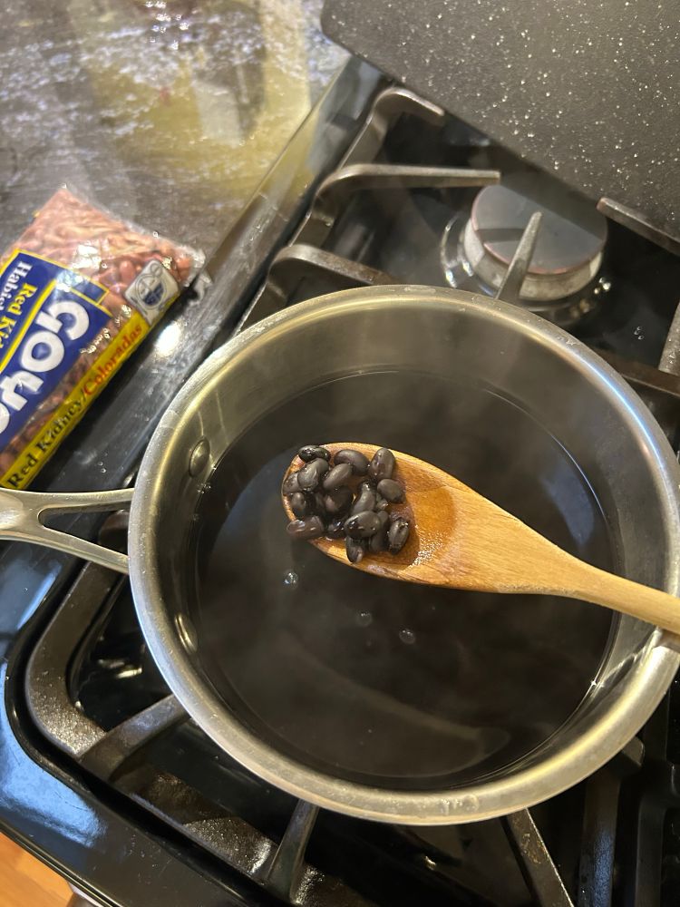 Pot filled with steaming water on stove with spoon filled with cooked beans