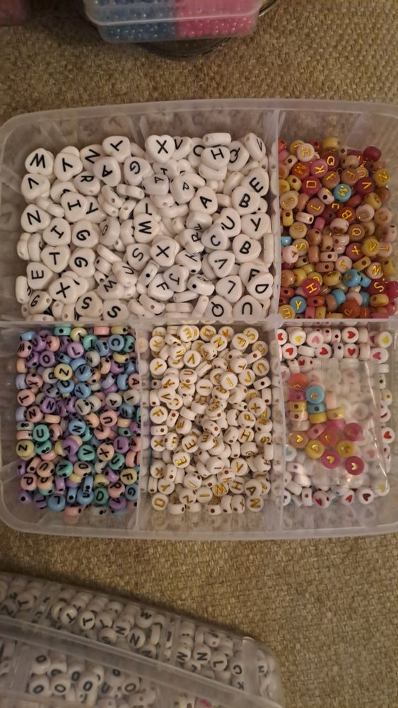 White, heart shaped beads with black letters. Colorful, round beads with golden colored letters. Pastel colored, round beads with black letters. White, round beads with gold letters. White and different colorful, round beads with different colored hearts in them