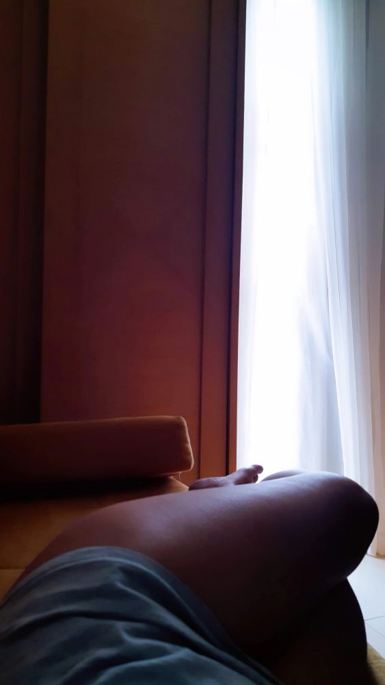 Foto deitada com as pernas cruzadas em frente a um armário. Ao lado, uma varanda. 