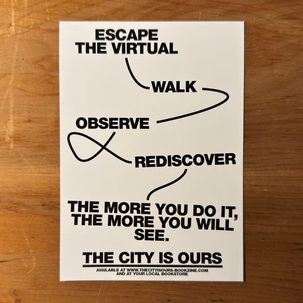 A postcard on a wooden surface with the words: Escape the virtual—walk—observe—rediscover—the more you do it, the more you will see. The City Is Ours.