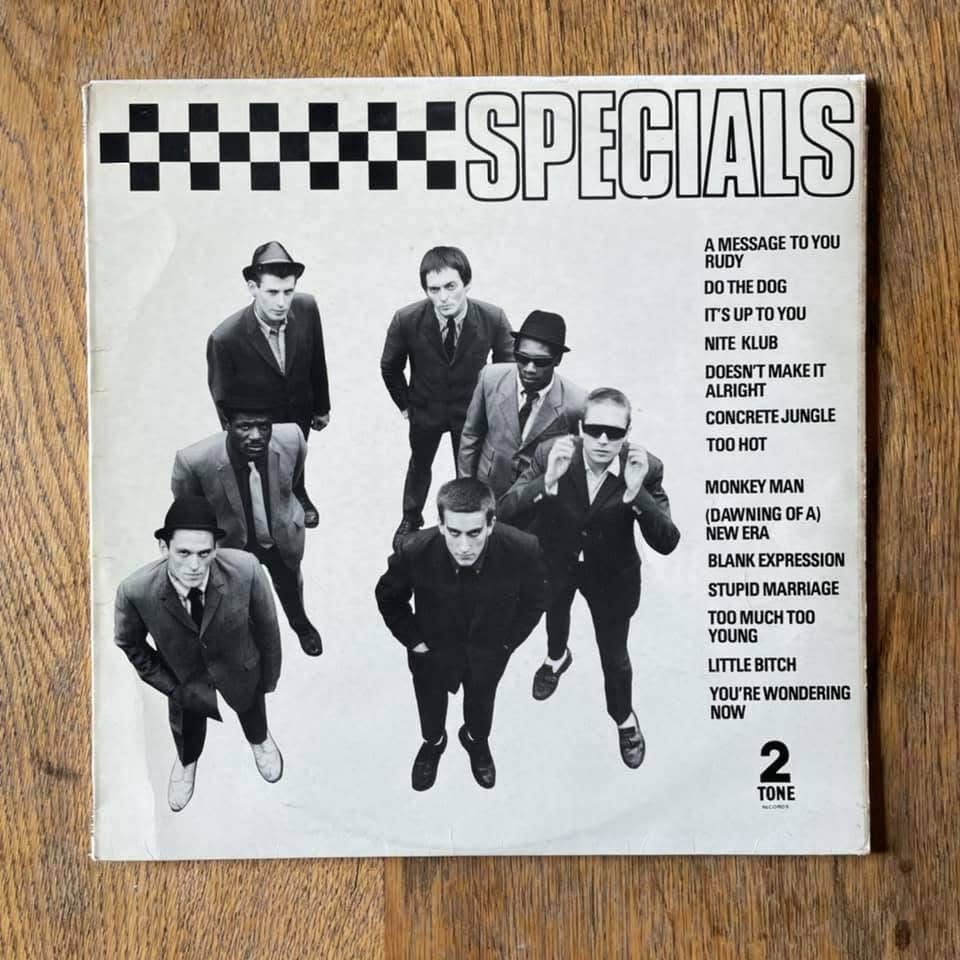A black and white record sleeve with 7 men standing looking up, the word Specials at the top next to black and white squares, and a track listing down the right hand side