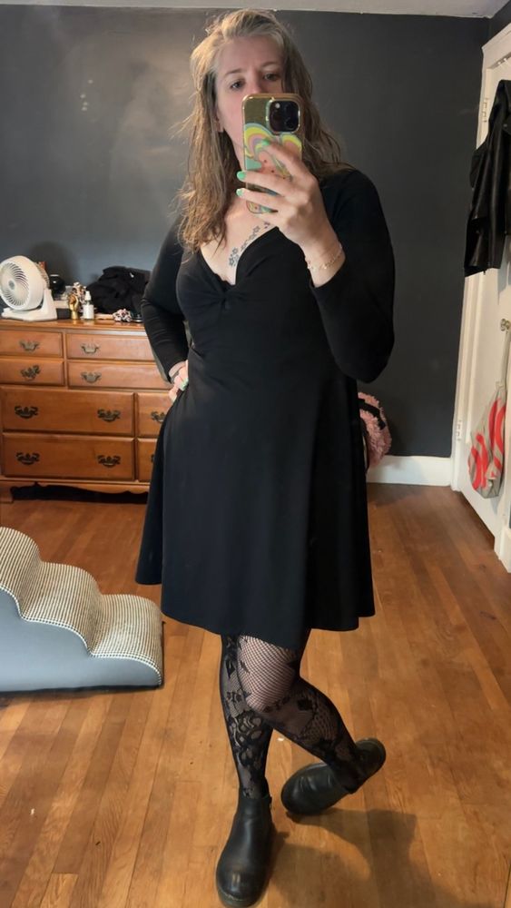 Dahlia wearing a black dress, fishnets and Chelsea boots 