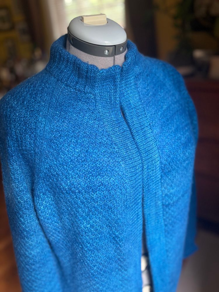 A hand-knit cardigan displayed on a dress form. The pattern is the “Old Fashioned” cardigan by Max the Knitter, made with Malabrigo Worsted yarn in the rich, vibrant “Taureg” colorway—a deep, tonal blue. The sweater features a textured stitch pattern, ribbed collar, and open front design. Soft natural light highlights the texture and color, showcasing the craftsmanship and cozy feel of the garment.