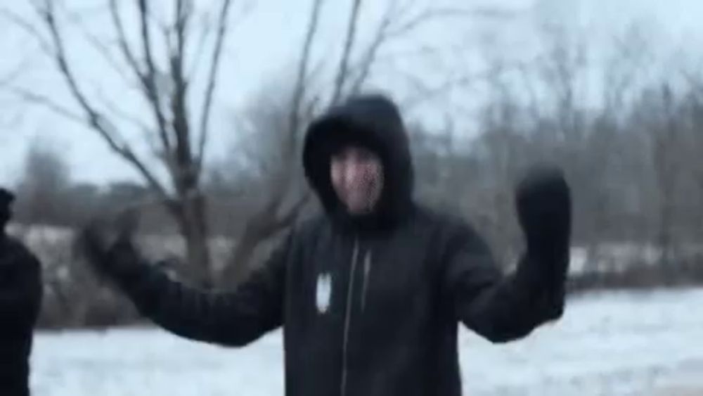 a man in a hooded jacket and mittens is standing in the snow .