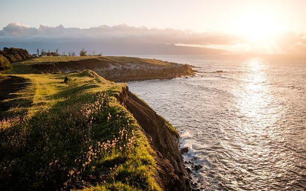 Background photo shows a green peninsula bordered by the sea, the sun setting.