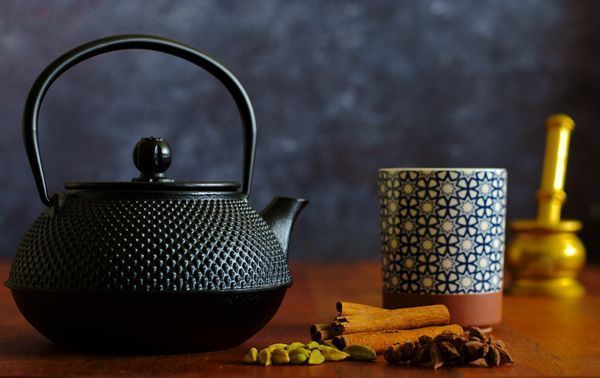 Background shows a decorative black Japanese styled Tetsubin Cast Iron Teapot and a handle-less tea mug resting on a redwood table.