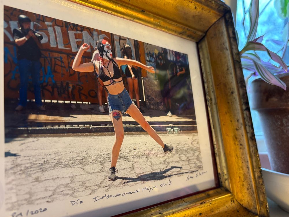 La photo d'un.e manifestant.e portant un masque dans un vieux cadre doré. La personne s'apprête à lancer des pierres.