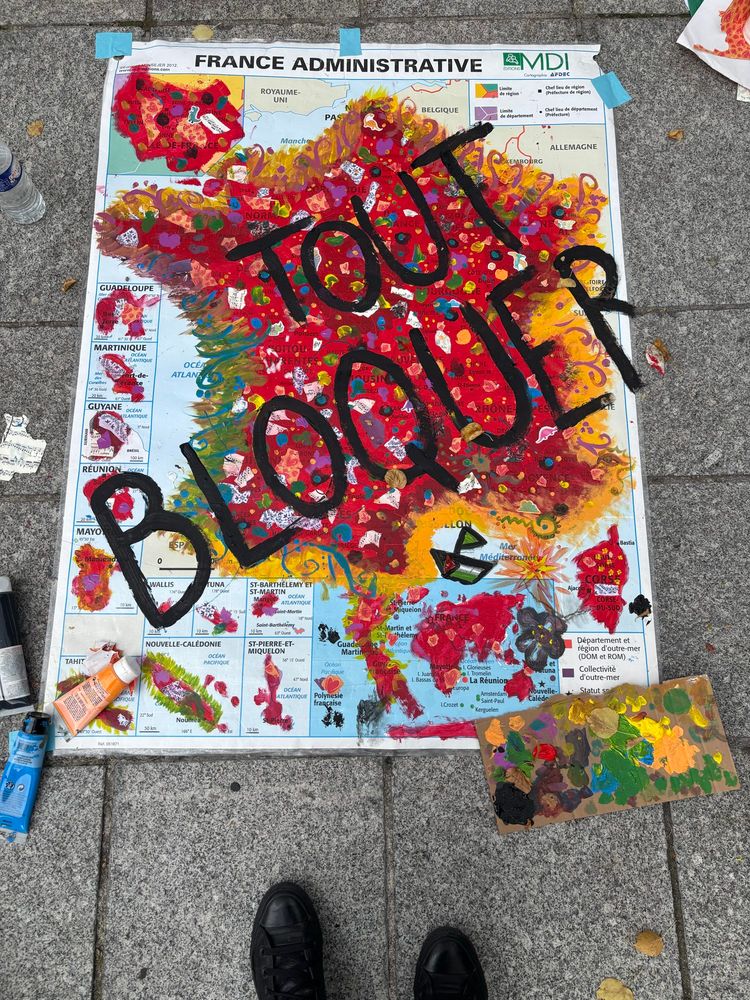 Œuvre collective : une carte de France posée au sol, repeinte, fond rouge et en grosses lettres noires « Tout bloquer »