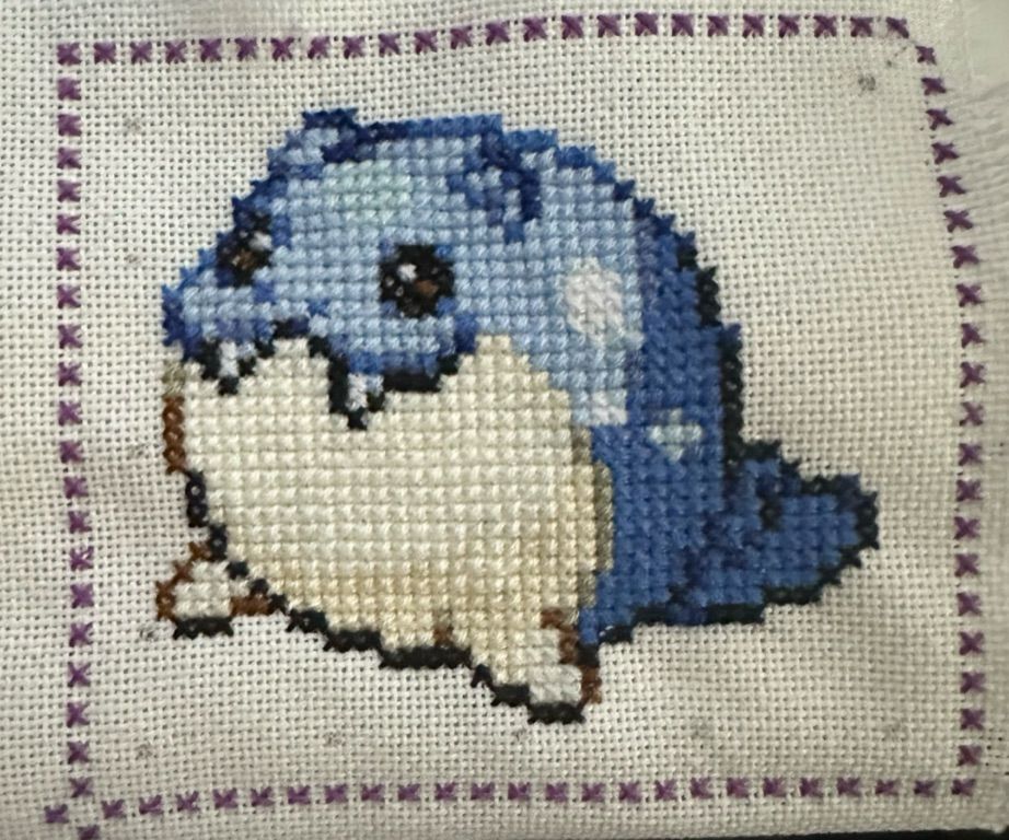 Spheal, cross stitch, with a purple dotted border. I forgot to erase the pencil marks I used to not lose my place
