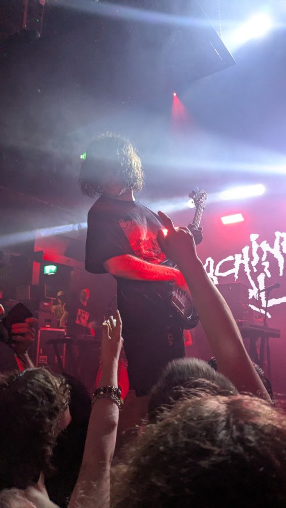 A photo of machine girl's front lman playing bass on stage, with arms reaching up to the stage 