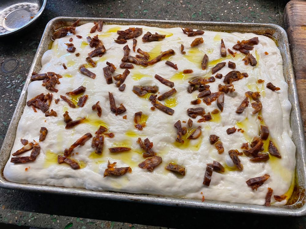 Focaccia dough in a sheet pan with chorizo scattered on top 
