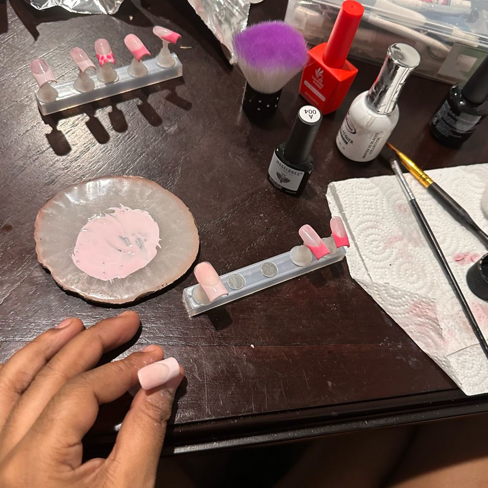 Snapshot of a hand of a person while making press on nails in shades of pink with red and pink tips. 