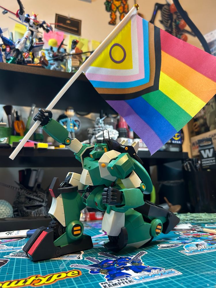 Picture of the Real Robot Revolution Walker Gallia in a kneeling pose holding up a pride flag 🏳️‍🌈 🏳️‍⚧️