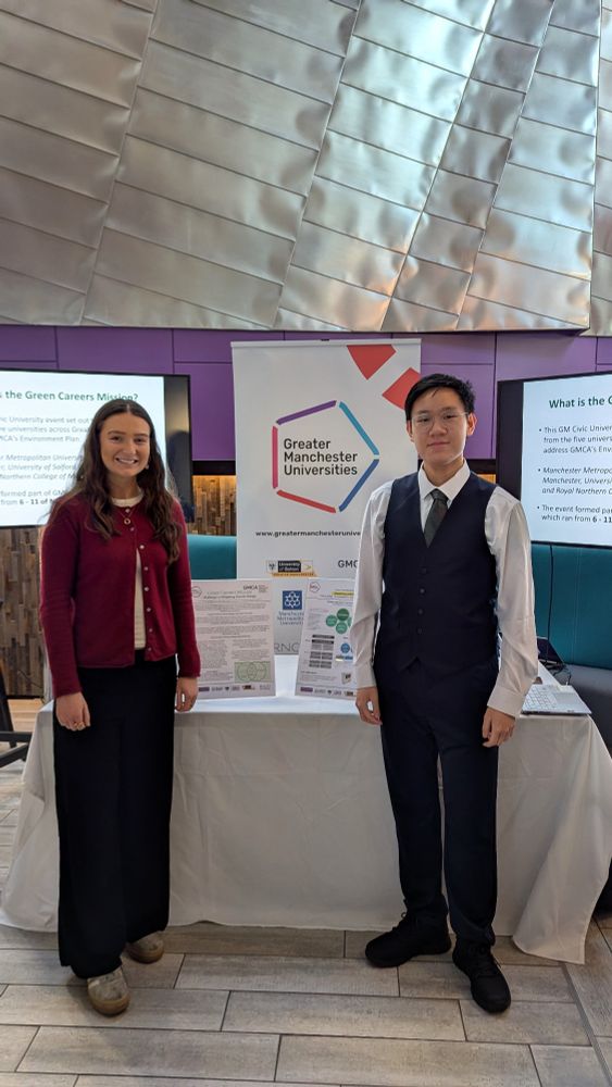 Two students are standing in front of an exhibition stand for Greater Manchester Universities 