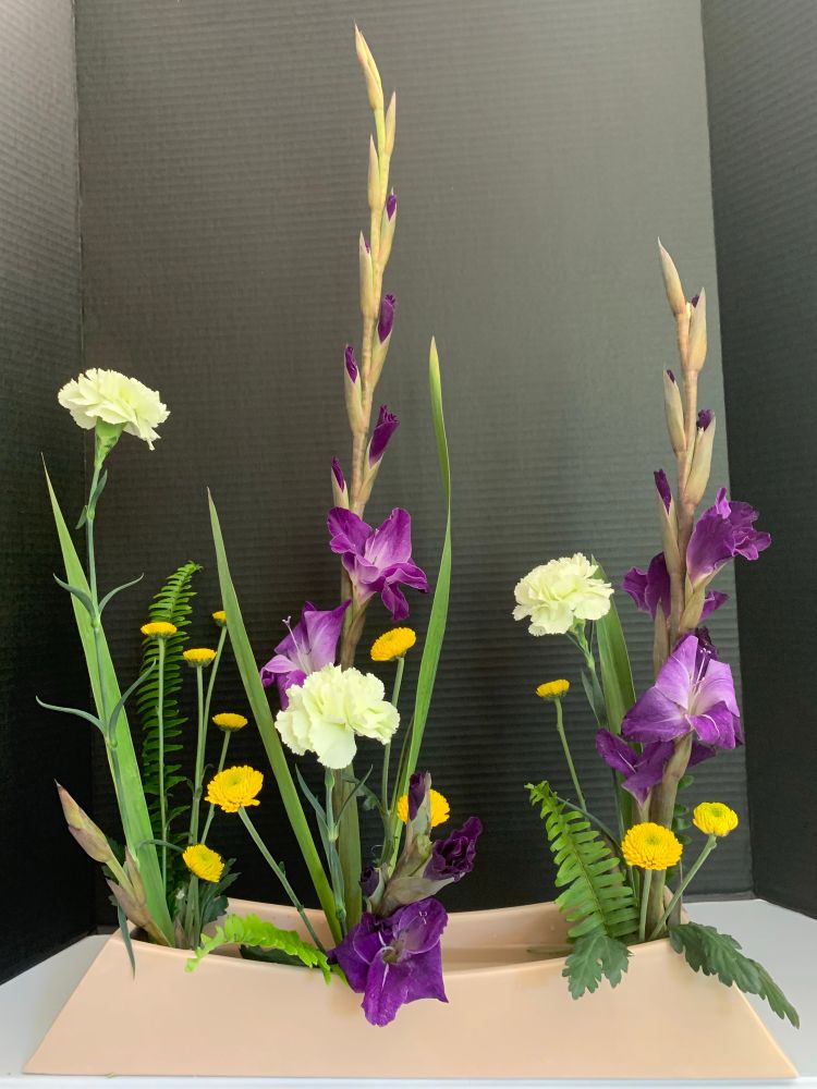 Three arrangements in the one-row form of the O’Hara school of ikebana, each composed of purple gladiolus, white carnations, small yellow mums, and ferns.