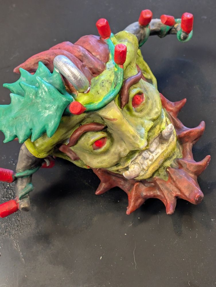 A grinning Krampus head, sculpted and painted with Xmas lights around the horns and mistletoe in his hair.