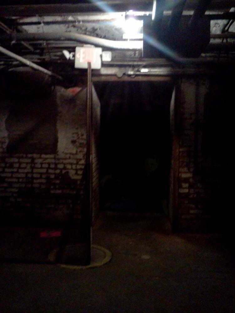 A low quality picture of a badly lit basement showing a dark doorway. Cheez-It crackers™ have been spread out on the floor. My uncle may also be there somewhere in the darkness.