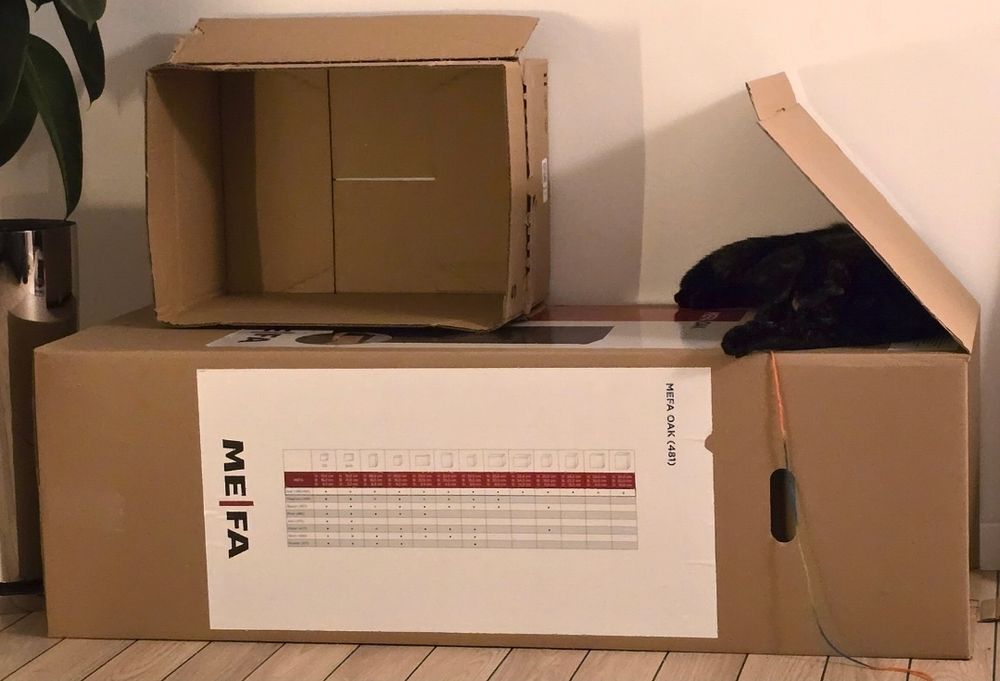 My cat is laying on top of a very large rectangular box which is laying horizontally on the floor, she has wedged herself under the flap of the box to create a little tent. A smaller square box is sitting on top of the larger box, making a cat fort