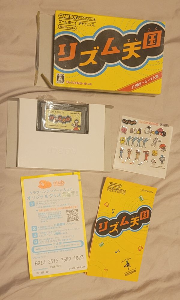 A photo of the game Rhythm Tengoku (Rhythm Heaven) for the Game Boy Advance, including the box, instruction booklet, sticker sheet, and other inserts