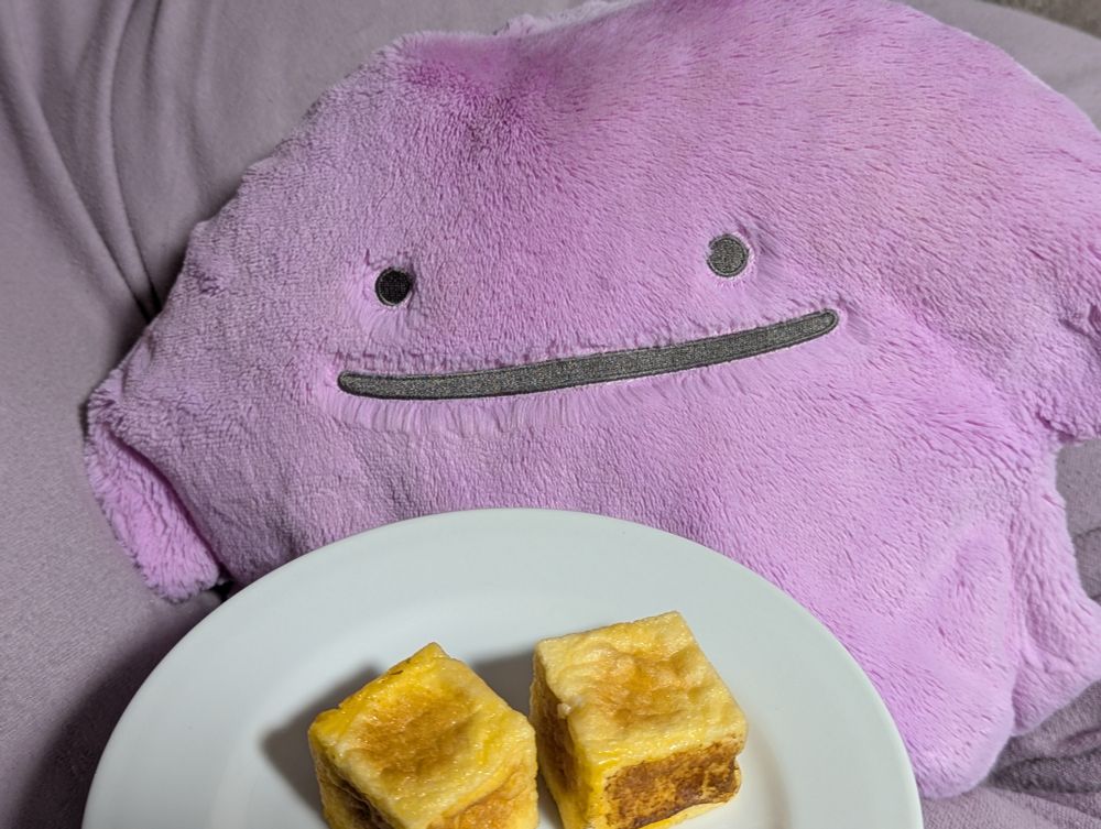 厚揚げや玉子焼きのように見える和菓子を怪訝に覗き込むふわふわメタモンぬいぐるみ