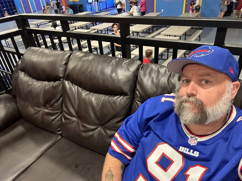 a tired fat adult on a super comfy couch at a trampoline park watching kids break their necks 