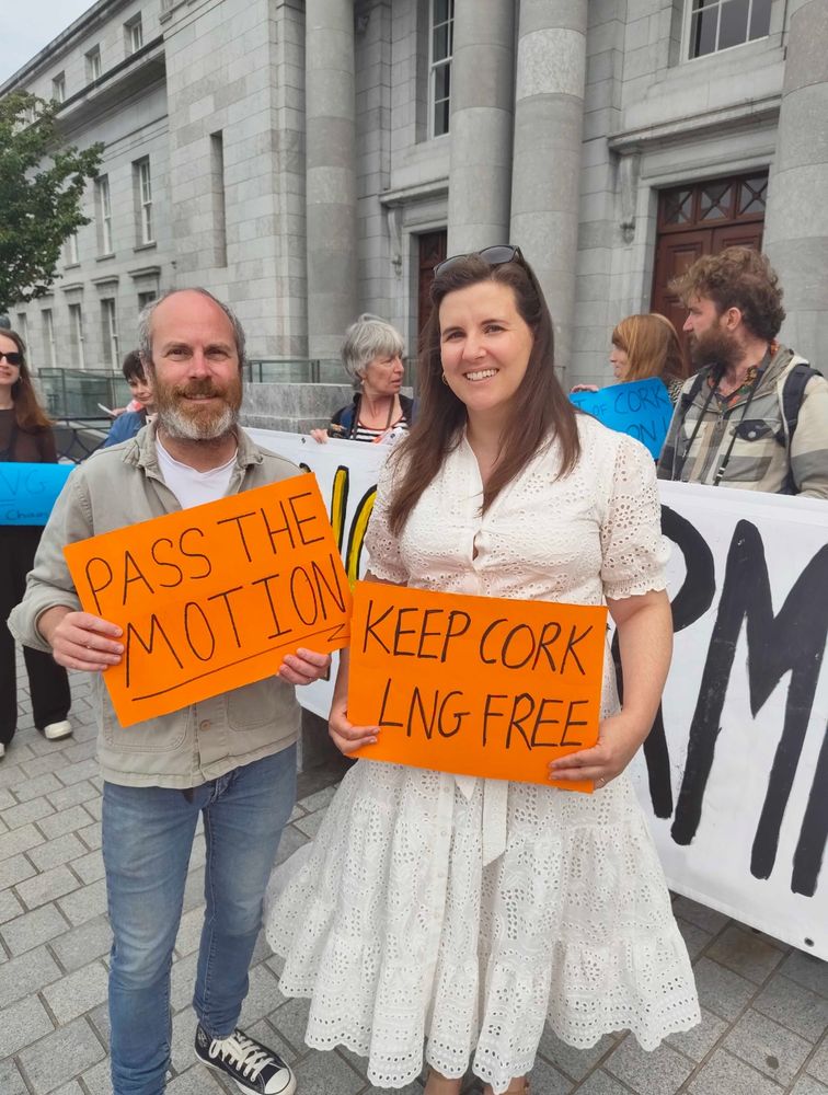 Two local Councilors holding posters and smiling, in front of the anti-LNG demonstration outside Cork City Hall 