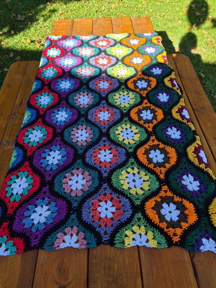 A funky crocheted blanket is spread out on a picnic table