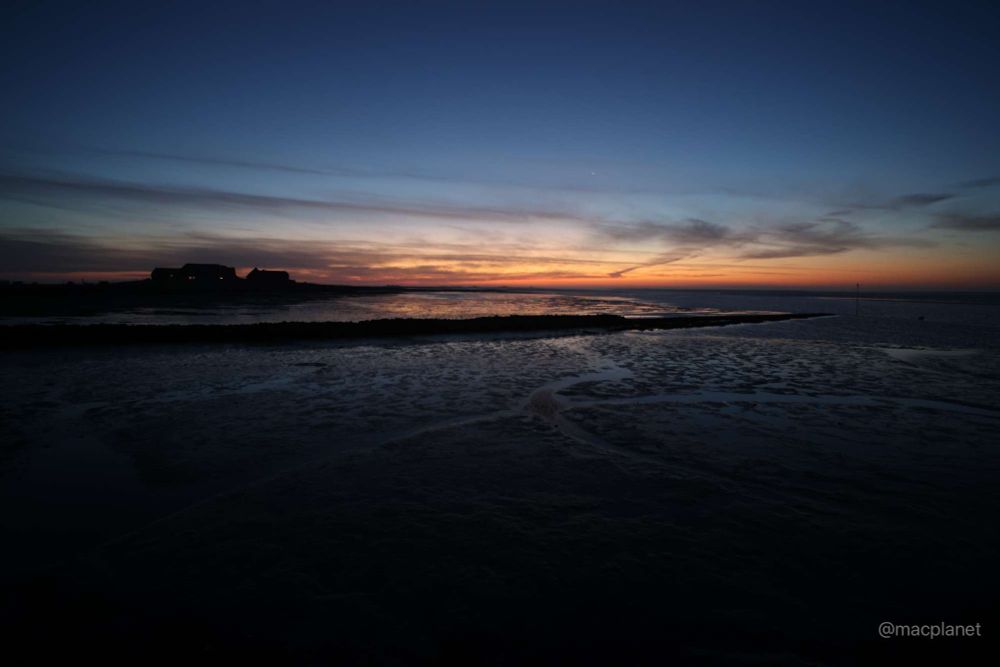 Dramatische Morgendämmerung über dem Watt, links im Bild eine Warf.