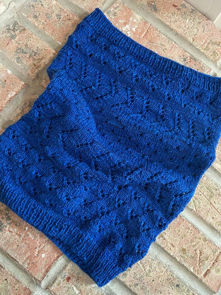 A bright blue lace cowl lays on a brick background 