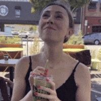 a woman in a black tank top is drinking a smoothie through a straw