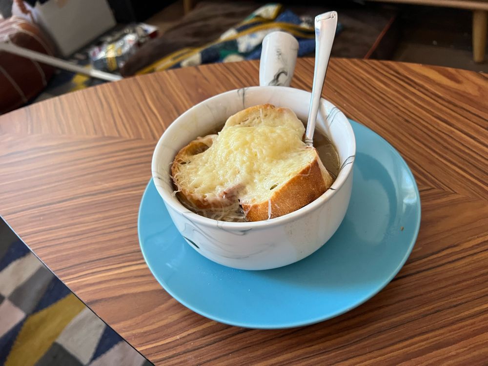 A picture of French onion soup, broiled, with melted Gruyère cheese, with slices of toasted baguette 