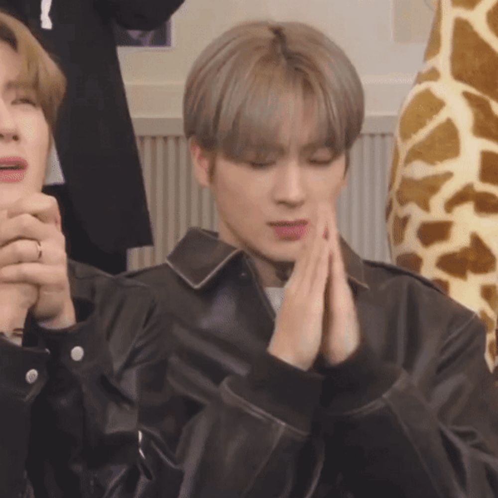 a man in a leather jacket is praying with his hands folded in front of a stuffed giraffe .