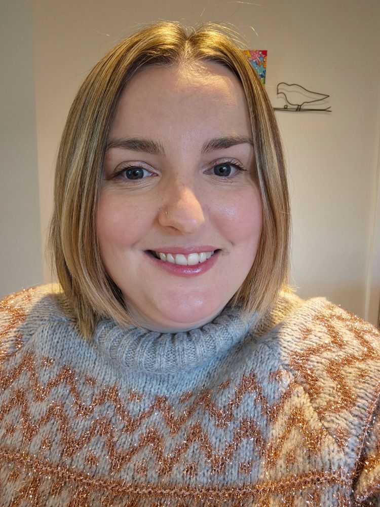 Picture is a selfie of me in a jumper, wearing makeup and showing off my new haircut/colour.