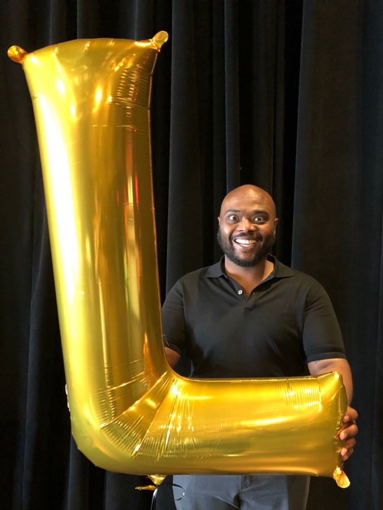 Chuck Taylor holding up a huge inflatable L