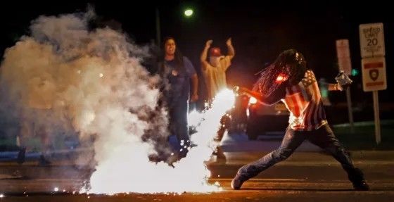 American Hero Edward Crawford throws back a chemical weapon canister that was fired at him while walking home from a convenience store. He is throwing it at Fascist military forces that occupied his neighborhood at the behest of President Barack Obama. Crawford was murdered later by the militarized law enforcement forces under president Obama.