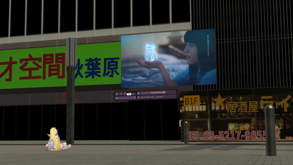 ビデオゲームVRChat。「オ空間秋葉原」と書かれていることが見えるビル。地面に座ってビデオプレイヤーを見ている長い金髪の少女。