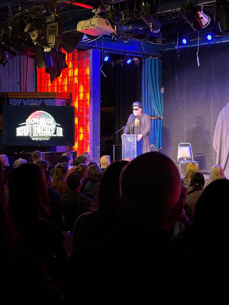 Comedian pretends to be Elon Musk on stage at a comedy show. 