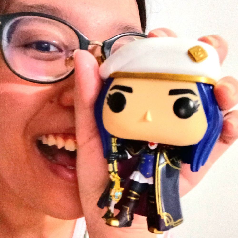 Anna smiling while holding the Caitlyn Funko Pop in front of her face.